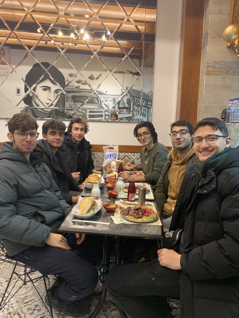 Abdullah and six friends around a restaurant table in Ankara, a large mural behind them.