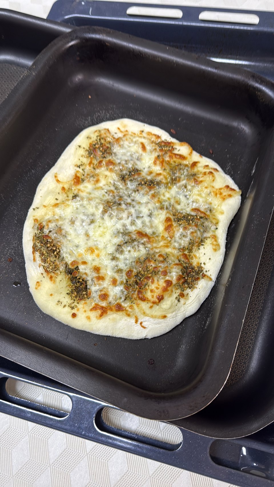 A flatbread baked at home, blistered and cheese-topped, fresh out of the pan.