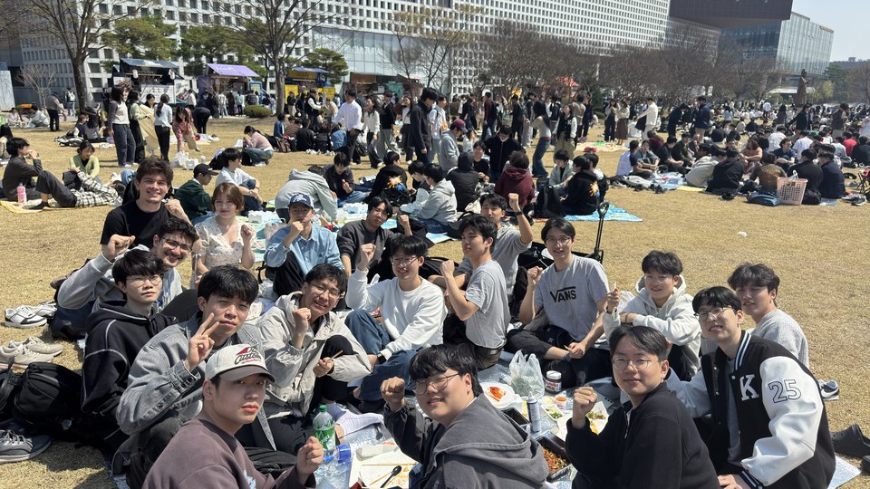 A large crowd of students sitting out on the KAIST campus lawn on a bright day.