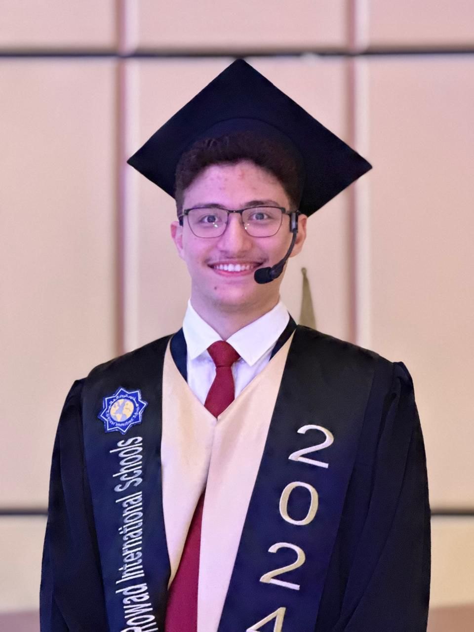 Abdullah in cap and gown with a 2024 sash and a headset microphone, hosting his own graduation ceremony.